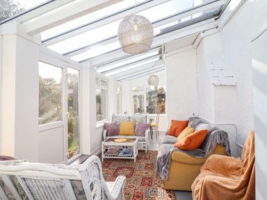 A sunroom with white wicker furniture a yellow couch orange and purple cushions a patterned rug and glass ceiling at The Flat At Brwyn in Brynford