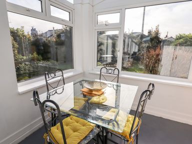 A dining area with a glass table and four metal chairs with yellow cushions by windows at The Flat At Brwyn in Brynford