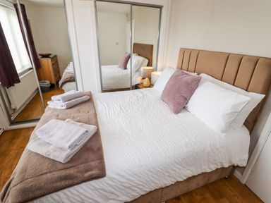 A bedroom with a double bed a brown headboard white bedding folded towels on a blanket bedside tables with lamps and a mirrored wardrobe at The Flat At Brwyn in Brynford