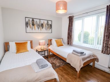 A bedroom with two single beds a lamp on a nightstand and a window with vertical blinds at The Flat At Brwyn in Brynford