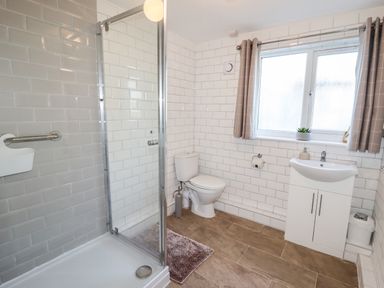 A bathroom with a shower enclosure toilet sink with cabinet and window with curtains at The Flat At Brwyn in Brynford