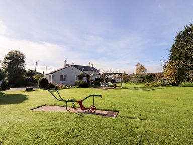 A garden with a lawn and a vintage gardening tool with a house and seating area in the background at The Flat At Brwyn in Brynford