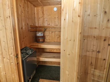 A wooden sauna room with benches a bucket with a ladle sauna stones and a thermometer on the wall at Awel Y Llan in Llanfair