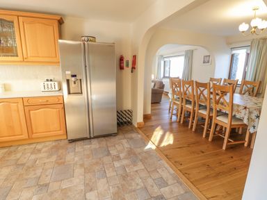 A kitchen with wooden cabinets a stainless steel refrigerator and a dining area with a large table and wooden chairs at Awel Y Llan in Llanfair