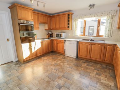 A kitchen with wooden cabinets a dishwasher a microwave an oven and tiled floor at Awel Y Llan in Llanfair