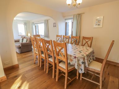 A dining room with a wooden table covered with a starfish patterned tablecloth and wooden chairs next to an archway leading to a living room at Awel Y Llan in Llanfair