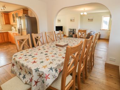 A long dining table with starfish patterned tablecloth and wooden chairs in an open plan kitchen and living area at Awel Y Llan in Llanfair