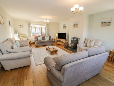 A living room with sofas a TV wood stove and coffee table at Awel Y Llan in Llanfair