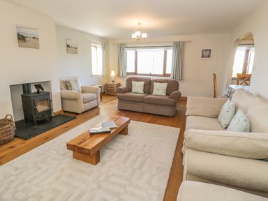 A living room with sofas a wooden coffee table a wood stove and windows at Awel Y Llan in Llanfair