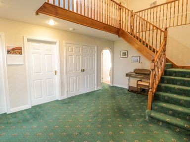 A hallway with staircase wooden railing green patterned carpet a keyboard and chair near the wall at Awel Y Llan in Llanfair