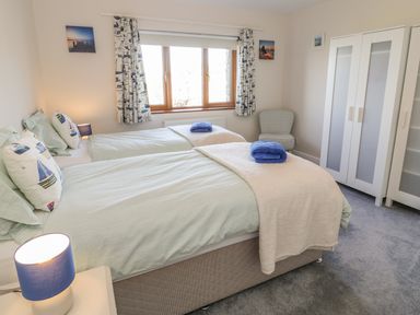 A bedroom with two single beds with blue and white bedding a window with curtains a white wardrobe and a chair at Awel Y Llan in Llanfair