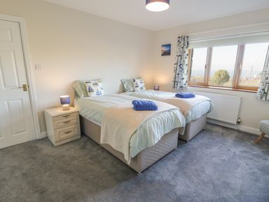 A bedroom with two single beds bedside tables lamps and a window with curtains at Awel Y Llan in Llanfair