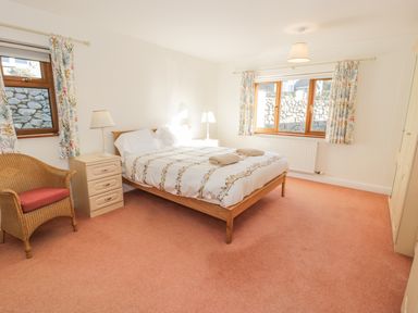 A bedroom with a double bed two bedside tables with lamps a wicker chair and floral curtains at Awel Y Llan in Llanfair
