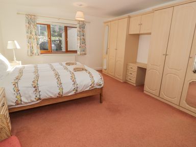 A bedroom with a bed beside a window and built in wardrobes with a desk area at Awel Y Llan in Llanfair