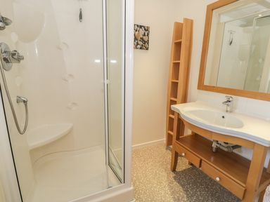 A bathroom with a corner shower unit a wooden vanity with a sink and a mirror and a wooden shelving unit at Awel Y Llan in Llanfair