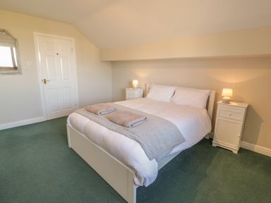 A bedroom with a double bed white bedside tables lamps and towels at Awel Y Llan in Llanfair