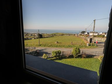A view through a window showing a fenced grassy field road poles houses and the sea at Awel Y Llan in Llanfair