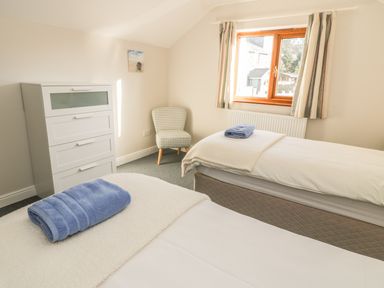 A bedroom with two single beds with blue towels on them a white chest of drawers and a patterned chair at Awel Y Llan in Llanfair