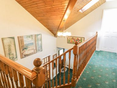 A staircase with wooden banisters and green carpet with patterned design at Awel Y Llan in Llanfair