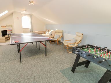 A game room with a table tennis table foosball table chairs a sofa and a small television at Awel Y Llan in Llanfair