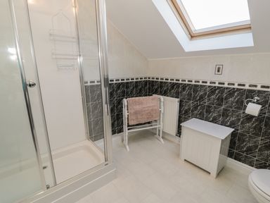 A bathroom with a shower enclosure a towel rack a white cabinet and a skylight at Awel Y Llan in Llanfair