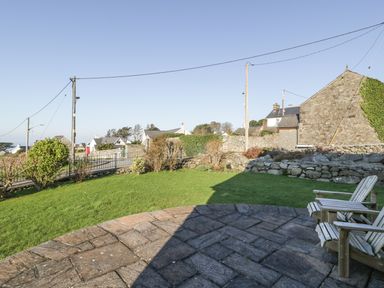A grass garden with stone paving and wooden chairs near stone houses at Awel Y Llan in Llanfair