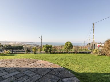 A garden with a stone patio and bushes overlooking fields and the sea at Awel Y Llan in Llanfair