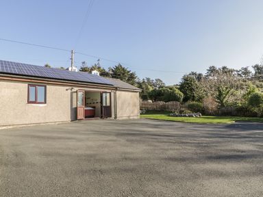 A building with solar panels on the roof and an open door next to a driveway and garden at Awel Y Llan in Llanfair