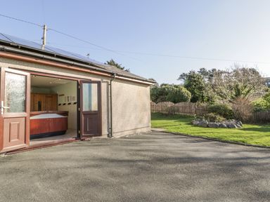 An outdoor area with an open double door leading to a room with a hot tub and a garden with grass and shrubs at Awel Y Llan in Llanfair