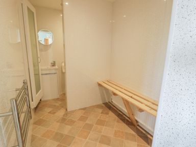 A room with tiled floor a wooden bench a heated towel rail and a door leading to a sink with a round mirror at Awel Y Llan in Llanfair