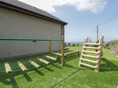 An outdoor wooden play structure with a climbing frame and slide in a garden with grass at Awel Y Llan in Llanfair