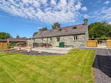 A stone cottage with a slate roof patio with picnic tables and a green lawn at Ffrwdd Galed Uchaf in Tregarth