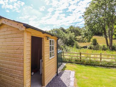 A wooden shed with an open door in a garden with grass trees and a wooden fence at Ffrwdd Galed Uchaf in Tregarth