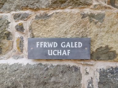 A stone wall with a rectangular gray sign reading Ffrwd Galed Uchaf at Ffrwdd Galed Uchaf in Tregarth