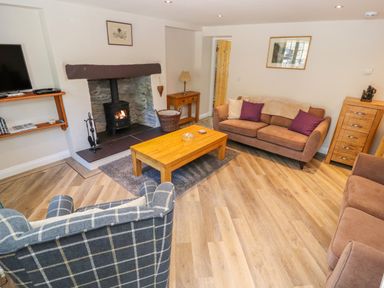 A living room with a fireplace a wooden coffee table two brown sofas a checkered armchair and a wooden cabinet at Ffrwdd Galed Uchaf in Tregarth