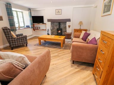 A living room with a fireplace a plaid armchair wooden coffee table and brown sofas at Ffrwdd Galed Uchaf in Tregarth