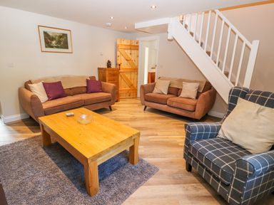 A living room with two brown sofas, a wooden coffee table on a rug, a patterned armchair, and a staircase at Ffrwdd Galed Uchaf in Tregarth