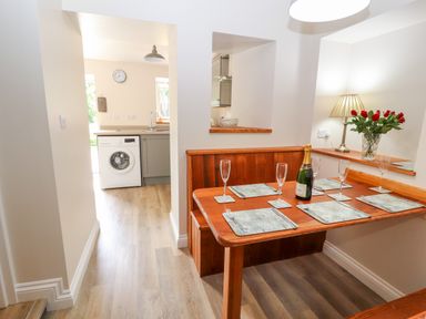 A dining area with a wooden table set with placemats glasses and a bottle next to a kitchen with a washing machine at Ffrwdd Galed Uchaf in Tregarth