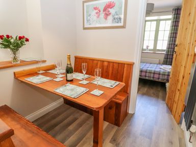 A dining area with a wooden table set with placemats glasses and a bottle next to a bedroom with a plaid bed at Ffrwdd Galed Uchaf in Tregarth