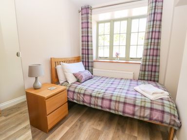 A small bedroom with a single bed with plaid bedding a wooden nightstand with a lamp and folded towels on the bed at Ffrwdd Galed Uchaf in Tregarth