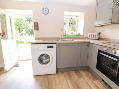 A kitchen with a washing machine under the counter a sink a toaster an oven and an open door showing an outside view at Ffrwdd Galed Uchaf in Tregarth