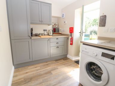 A kitchen with grey cabinets a kettle microwave washing machine and fire safety equipment at Ffrwdd Galed Uchaf in Tregarth