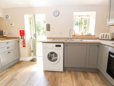 A kitchen with grey cabinets a washing machine a sink a toaster and an open door at Ffrwdd Galed Uchaf in Tregarth