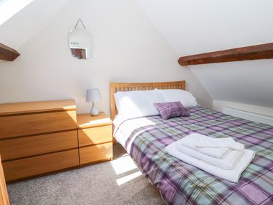 A bedroom with a wooden bed with a checkered duvet and folded towels on it a chest of drawers with a lamp and a wall mirror at Ffrwdd Galed Uchaf in Tregarth