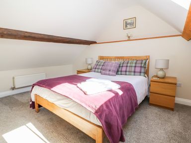 A bedroom with a wooden bed a purple blanket and plaid pillows two bedside tables with lamps and a framed picture on the wall at Ffrwdd Galed Uchaf in Tregarth