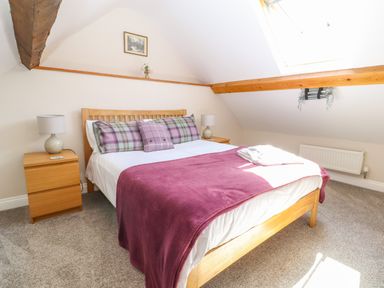 A bedroom with a wooden bed with purple bedding and two bedside tables with lamps at Ffrwdd Galed Uchaf in Tregarth