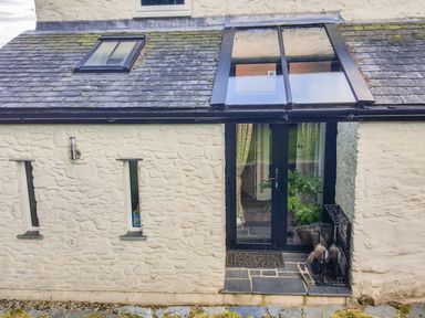 An exterior view of a stone wall with a glass door and skylights on a tiled roof at Rhydygaled in Llanrhaeadr-Ym-Mochnant