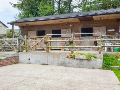 An outdoor stable building with wooden doors and a fenced area in front at Rhydygaled in Llanrhaeadr-Ym-Mochnant