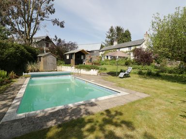 An outdoor swimming pool with a black shed and a small wooden building in a garden at Rhydygaled in Llanrhaeadr-Ym-Mochnant