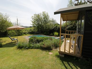 A backyard with a small pool lawn chairs an umbrella and a wooden porch at Rhydygaled in Llanrhaeadr-Ym-Mochnant